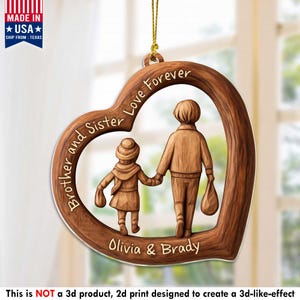 May include: A heart-shaped wooden ornament with the words "Brother and Sister Love Forever" and the names "Olivia & Brady." The ornament features a carved design of two figures holding hands. The ornament is hanging by a gold string.