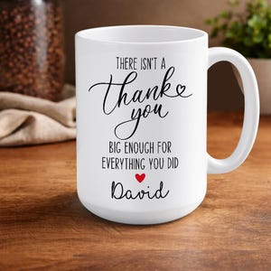 May include: A white ceramic mug with a black handle and the text "But First, Coffee" in a black, handwritten-style font. The mug is on a white surface.