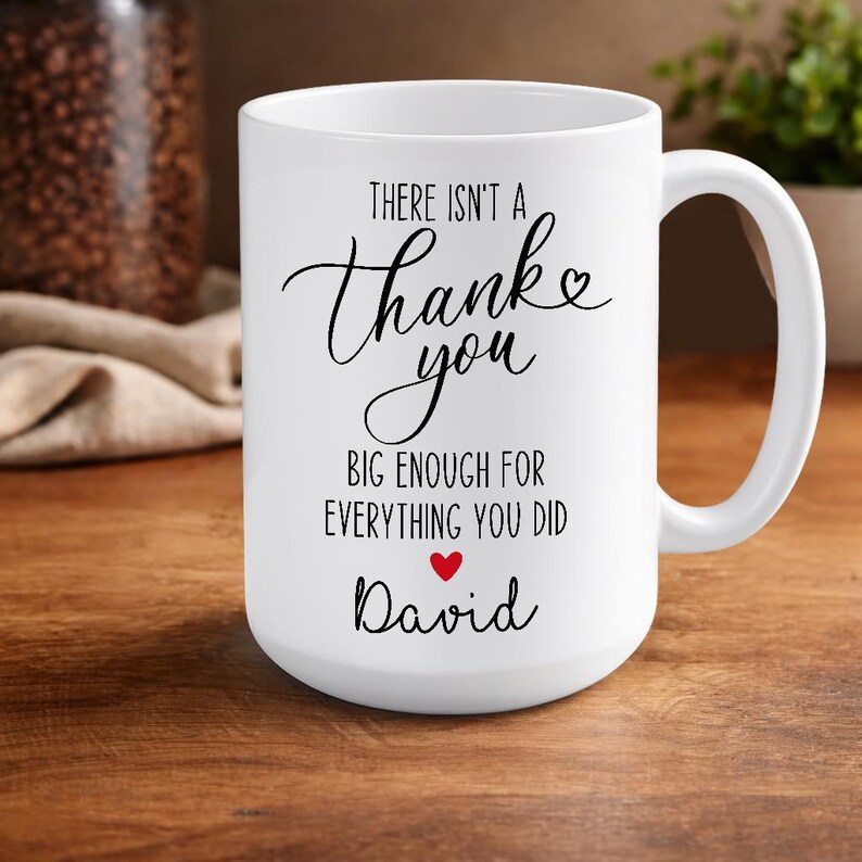 May include: A white ceramic mug with a black handle and the text "But First, Coffee" in a black, handwritten-style font. The mug is on a white surface.