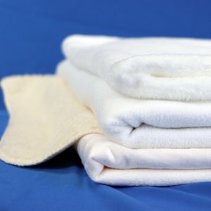 May include: A stack of four white towels, folded neatly, on a blue background. The top towel is folded over, creating a soft, fluffy texture.