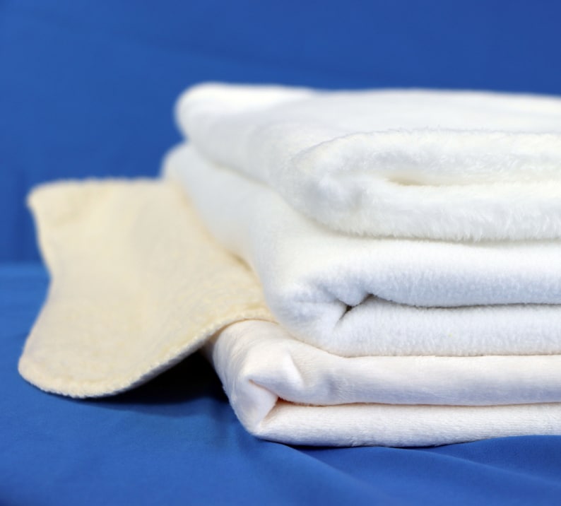 May include: A stack of four white towels, folded neatly, on a blue background. The top towel is folded over, creating a soft, fluffy texture.