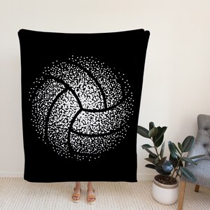 K&ouml;nnte beinhalten: Schwarze und wei&szlig;e Kuscheldecke mit einem wei&szlig;en Volleyball-Design aus Punkten. Der Volleyball befindet sich in der Mitte der Decke.