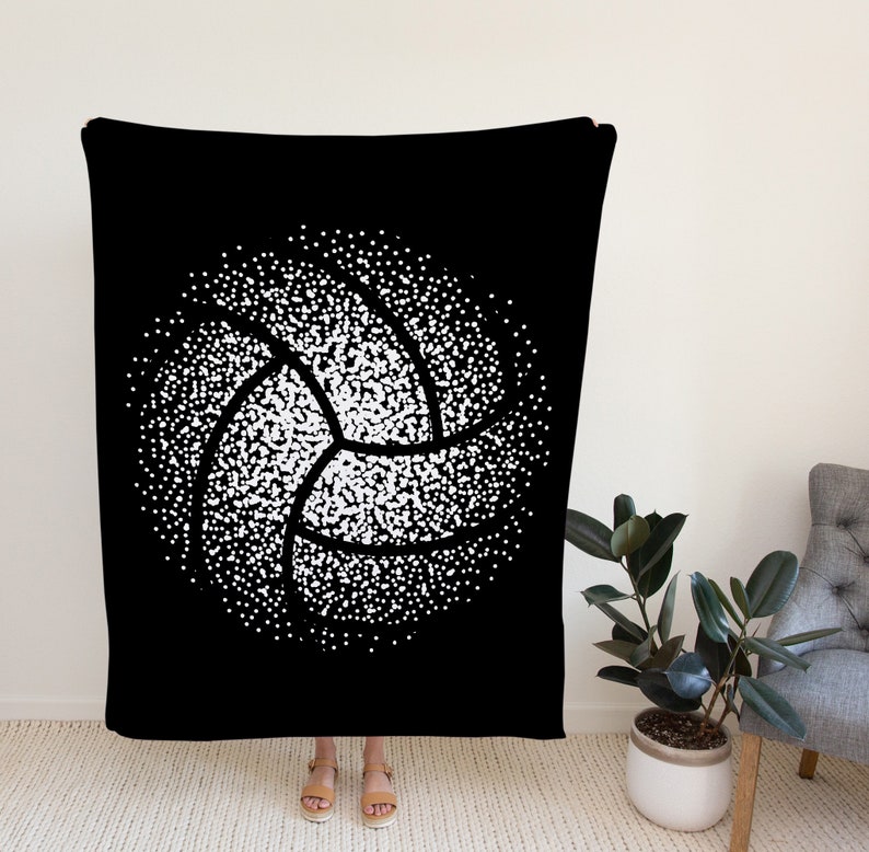K&ouml;nnte beinhalten: Schwarze und wei&szlig;e Kuscheldecke mit einem wei&szlig;en Volleyball-Design aus Punkten. Der Volleyball befindet sich in der Mitte der Decke.
