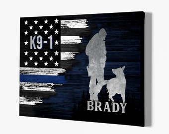 Op de afbeelding: Een zwart-blauwe Amerikaanse vlag met een dunne blauwe lijn, een silhouet van een politieagent en een hond, en de tekst "K9-1" en "BRADY".