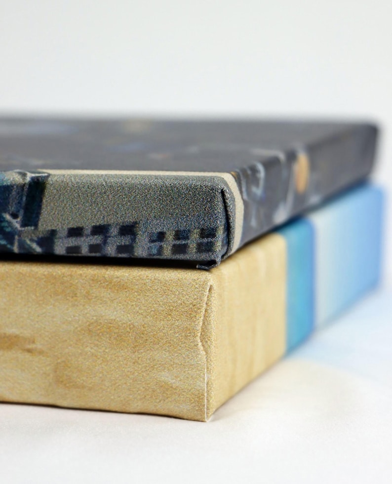May include: Two canvases stacked on top of each other. The top canvas has a dark blue and gray patterned design. The bottom canvas is a light beige color.