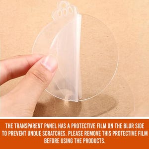 May include: A clear, round, adhesive sticker with a protective film on one side. The film is being peeled back to reveal the adhesive side of the sticker.