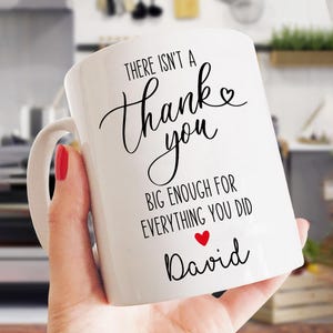 May include: White ceramic mug with a curved handle. The mug features black script that reads "There isn't a Thank you big enough for everything you did" with a red heart and the name "David".