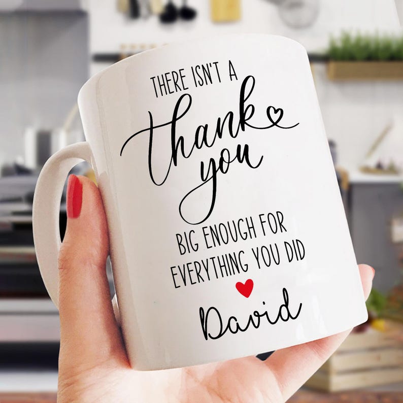 May include: White ceramic mug with a curved handle. The mug features black script that reads "There isn't a Thank you big enough for everything you did" with a red heart and the name "David".