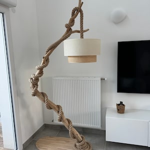 May include: A floor lamp made from a natural driftwood branch with a thick rope wrapped around it. The lampshade is a beige linen cylinder with a woven texture.