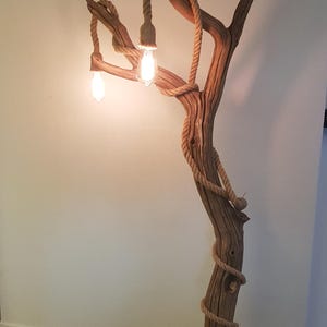 May include: A rustic floor lamp made from a natural branch with rope accents and three light bulbs. The lamp is lit and casting a warm glow.