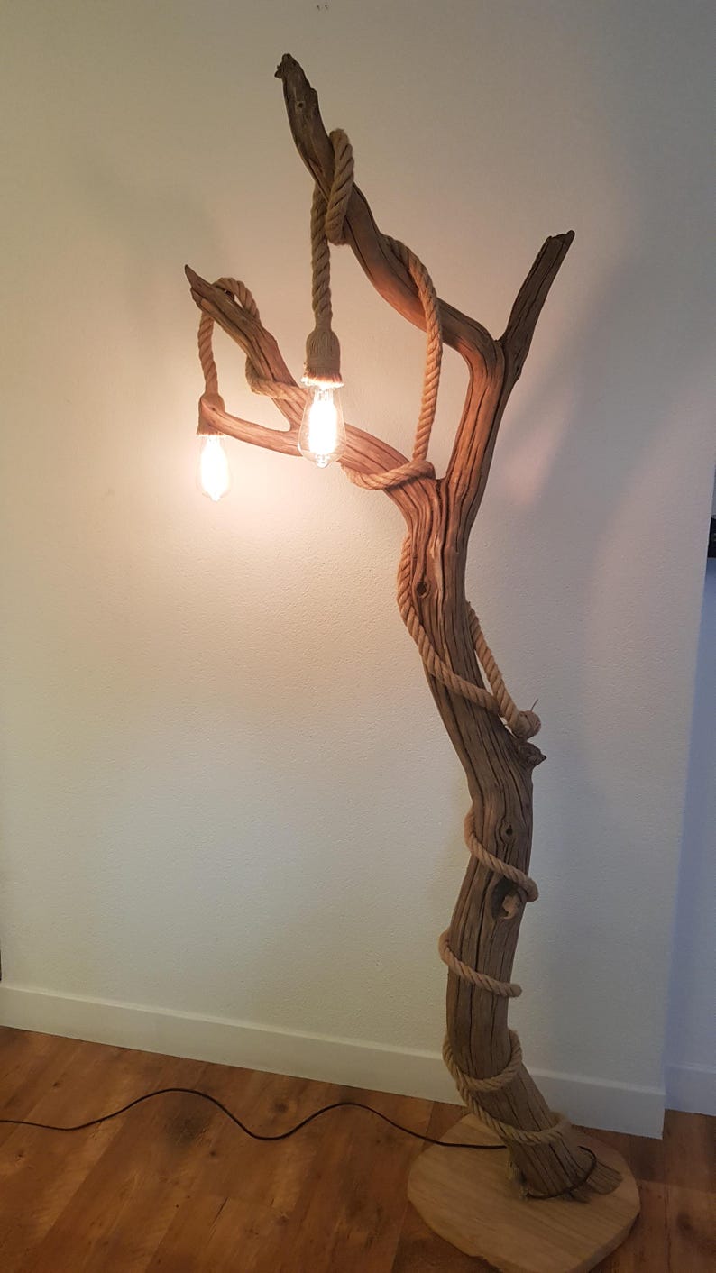 May include: A rustic floor lamp made from a natural branch with rope accents and three light bulbs. The lamp is lit and casting a warm glow.
