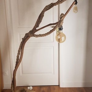 May include: A floor lamp made from a natural branch wrapped in rope with two light bulbs. The lamp is standing on a wooden base.