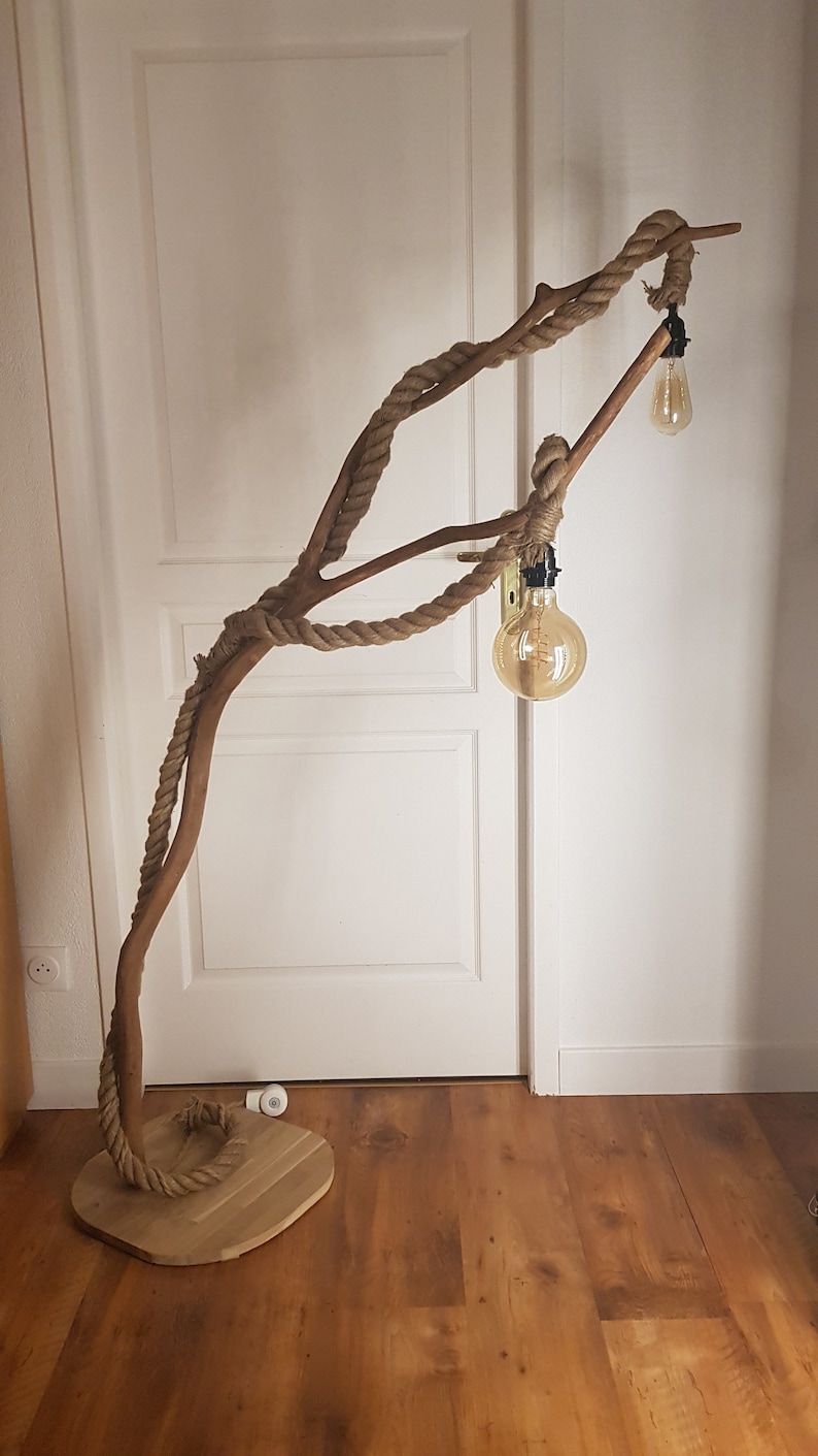 May include: A floor lamp made from a natural branch wrapped in rope with two light bulbs. The lamp is standing on a wooden base.
