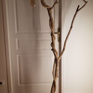 May include: A floor lamp made from a natural branch wrapped in rope with a light bulb at the top. The branch is attached to a wooden base.