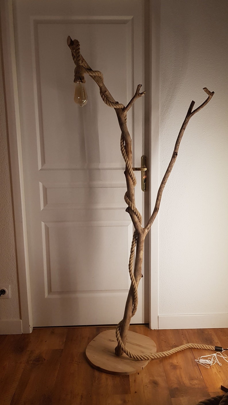May include: A floor lamp made from a natural branch wrapped in rope with a light bulb at the top. The branch is attached to a wooden base.