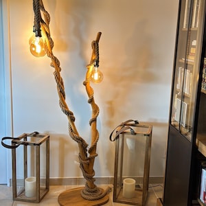 May include: A wooden floor lamp with a unique design featuring two branches wrapped in rope and topped with light bulbs. The lamp is next to two wooden lanterns with glass panels.