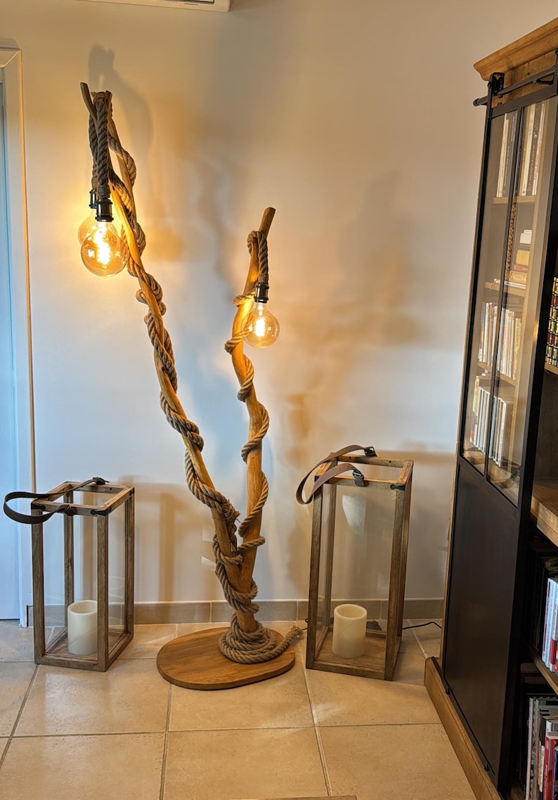 May include: A wooden floor lamp with a unique design featuring two branches wrapped in rope and topped with light bulbs. The lamp is next to two wooden lanterns with glass panels.