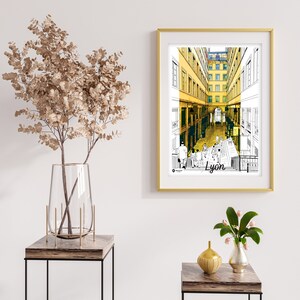 May include: A framed print of a black and white illustration of a street in Lyon, France. The buildings are yellow and the street is lined with people. The text "Lyon" is printed at the bottom of the print.
