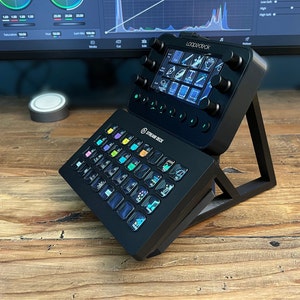 May include: A black Stream Deck XL with a black Loopdeck+ on top. The Stream Deck XL has a grid of 32 customisable buttons with colourful icons. The Loopdeck+ has a small LCD screen and several knobs and buttons.