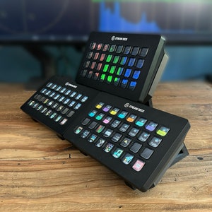 May include: Three black Stream Deck devices with customisable buttons and coloured icons. The devices are stacked on top of each other on a wooden surface.