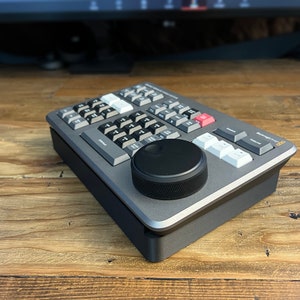 May include: A gray and black video editing control panel with a large knob and a variety of buttons. The panel is labeled "Blackmagic Design  -  DeckLink  -  8K Pro  -  SDI  -  Control Panel".