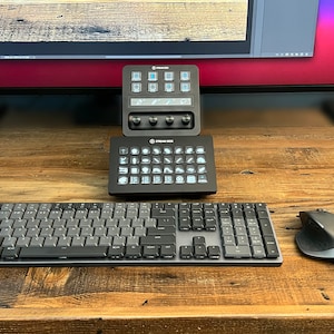 May include: A black keyboard with a gray keycap set, a black mouse, and two black control panels with white buttons and icons. The control panels are labeled "Stream Deck".