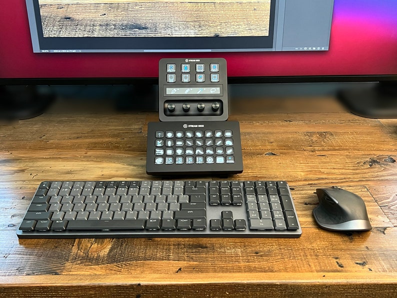 May include: A black keyboard with a gray keycap set, a black mouse, and two black control panels with white buttons and icons. The control panels are labeled "Stream Deck".