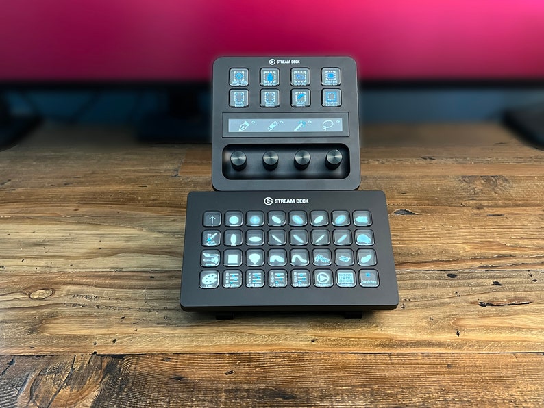 May include: Two black Stream Deck controllers with illuminated buttons and knobs. The top controller has nine buttons and three knobs. The bottom controller has 32 buttons.