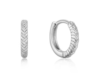 May include: Two silver-colored hoop earrings. Each earring has a braided design on the outer surface. The earrings are shown against a white background, with a slight reflection visible below.