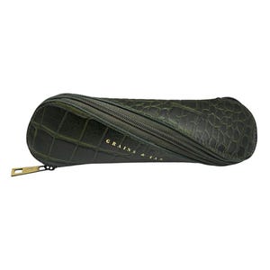 May include: A dark green, textured glasses case with a zip closure and gold-coloured zip pull. The case has a crocodile skin pattern and the words "GRAINS & IAN" are printed in gold.