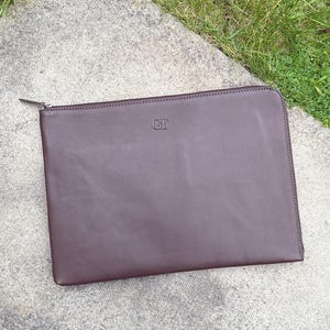 May include: A brown leather laptop sleeve with a zip closure and the initials "GT" embossed on the front.