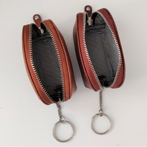 May include: Two brown leather zippered coin purses with keychains. The purses are open and the inside lining is black and white striped.