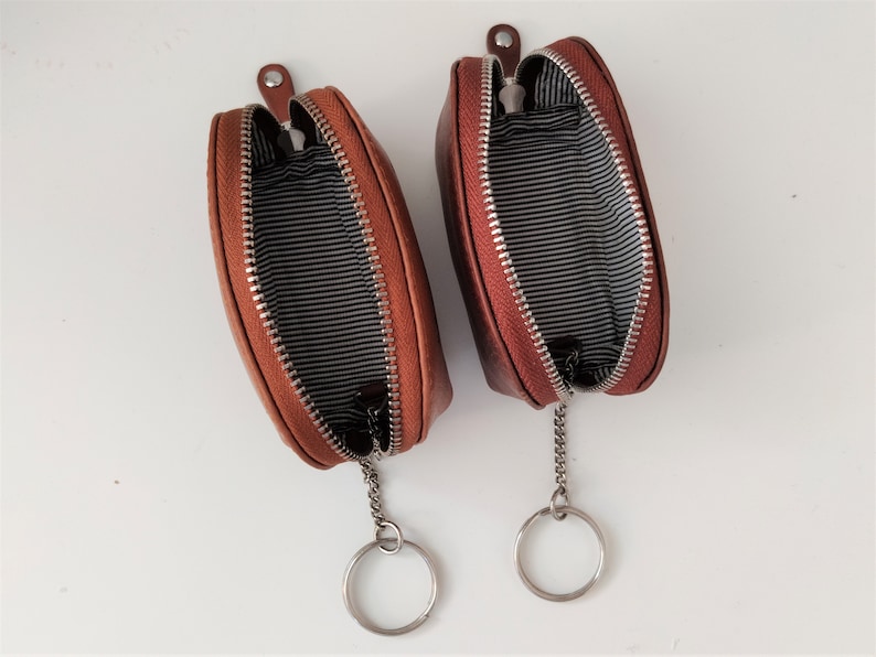 May include: Two brown leather zippered coin purses with keychains. The purses are open and the inside lining is black and white striped.