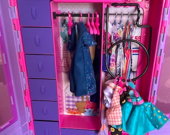 Puede incluir: Un armario de juguete de plástico rosa con un interior morado. El armario tiene una percha para colgar la ropa y un juego de cajones. El armario está abierto y el interior es visible.
