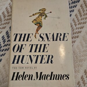 May include: A vintage book titled "The Snare of the Hunter" by Helen MacInnes. The cover features a map-like illustration of a figure with a spear. The title is in bold navy blue font, with the author's name below.