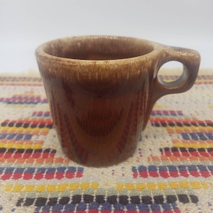 May include: A brown ceramic mug with a white rim and a brown handle. The mug has a mottled glaze with brown and red streaks.