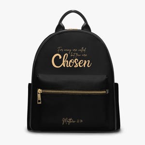 Puede incluir: Mochila negra con cremalleras y detalles dorados. El texto dorado "For many are called, but few are Chosen" está impreso en la parte delantera. El texto "Matthew 22:14" está impreso debajo.