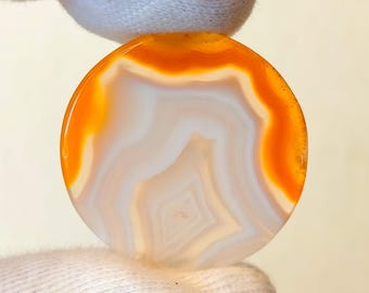 May include: A round, white agate stone with orange banding. The stone has a natural, polished finish.