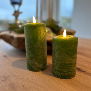 Könnte beinhalten: Zwei grüne Kerzen mit einer strukturierten Oberfläche sind angezündet und stehen auf einem Holztisch.