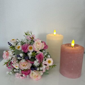 May include: A bouquet of pink and white flowers with a white pillar candle and a pink pillar candle, both with a flickering flame.