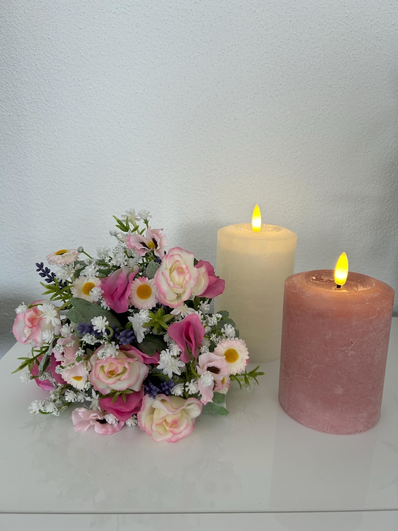 May include: A bouquet of pink and white flowers with a white pillar candle and a pink pillar candle, both with a flickering flame.