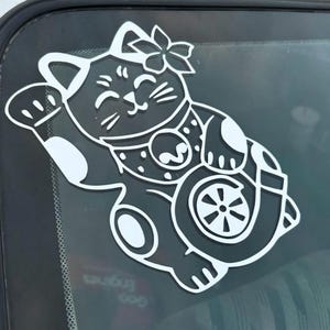 May include: White vinyl sticker of a cartoon lucky cat holding a turbocharger. The cat has a flower on its head and a happy expression.