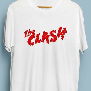 Może przedstawiać: Biała koszulka z nadrukowanym czerwonym logo "The Clash" z przodu.
