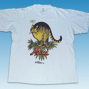 May include: White t-shirt with a cartoon cat wearing a surprised expression and the word "Wau!" above its head. The cat is standing on a green plant with the word "Maui" written in orange below it. The text "©Mitchum 1979" is at the bottom of the design.