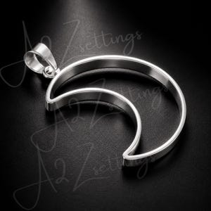 May include: A silver-colored pendant in the shape of a crescent moon. The pendant has a smooth, polished finish and a loop for a chain. The design features two curved lines, creating a layered effect. The background is black.