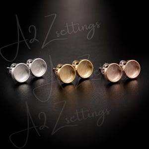 May include: A collection of earring settings in silver, gold, and rose gold. Each pair features a round bezel cup for setting stones or other embellishments. The earrings are displayed against a dark background, with the text "A2 Zsettings" in the background.