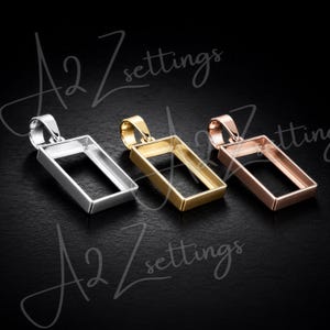 May include: Three rectangular pendant settings in silver, gold, and rose gold. Each setting has a loop for a chain and a recessed area for a stone or design. The settings are displayed on a dark background.