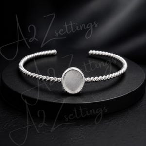 Può includere: Un bracciale a polsino argentato con un motivo a corda intrecciata. Presenta un'incastonatura ovale al centro, ideale per design personalizzati. Il bracciale è esposto su una superficie nera. Il testo "A2 Zsettings" è visibile sullo sfondo.