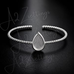 May include: Silver-toned open cuff bracelet with a teardrop-shaped setting. The bracelet features a twisted rope design. The setting is designed to hold a stone or other decorative element. The background is black.