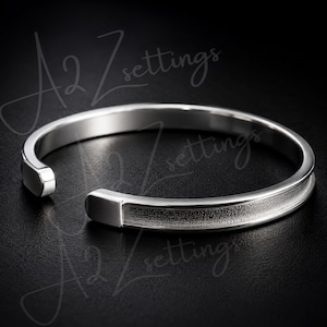 May include: A silver-toned open cuff bracelet featuring a smooth, polished finish on the edges and a textured, matte-finish center channel. The bracelet has rounded, solid ends and is marked with the text A2 settings overlaid on the image.
